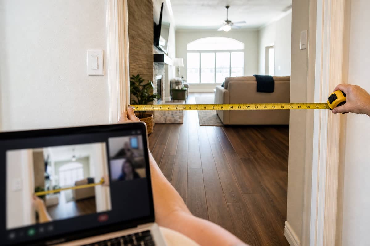 Tape measure across a wide interior doorway while a laptop shows the same opening on a video call.