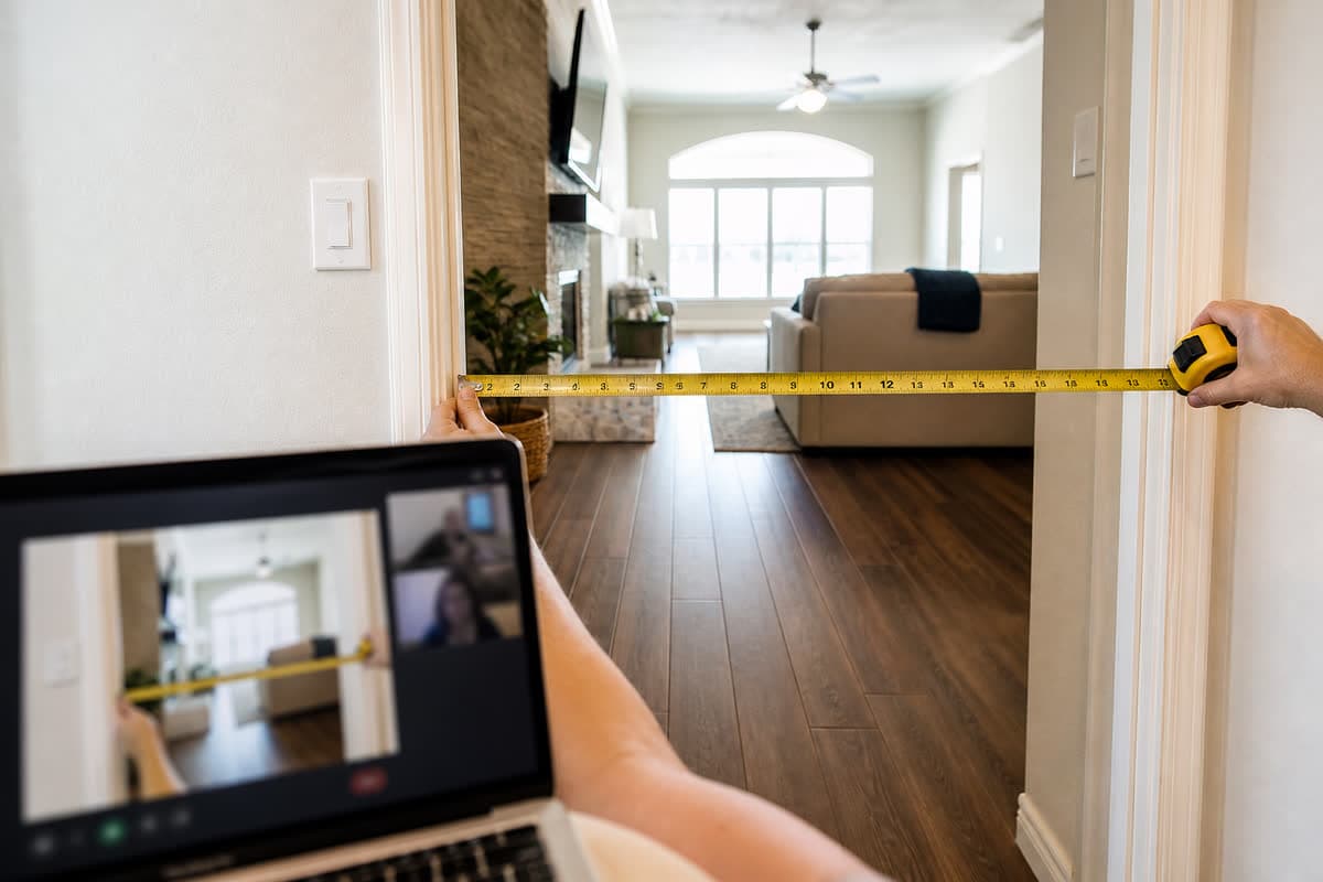 Tape measure across a wide interior doorway while a laptop shows the same opening on a video call.